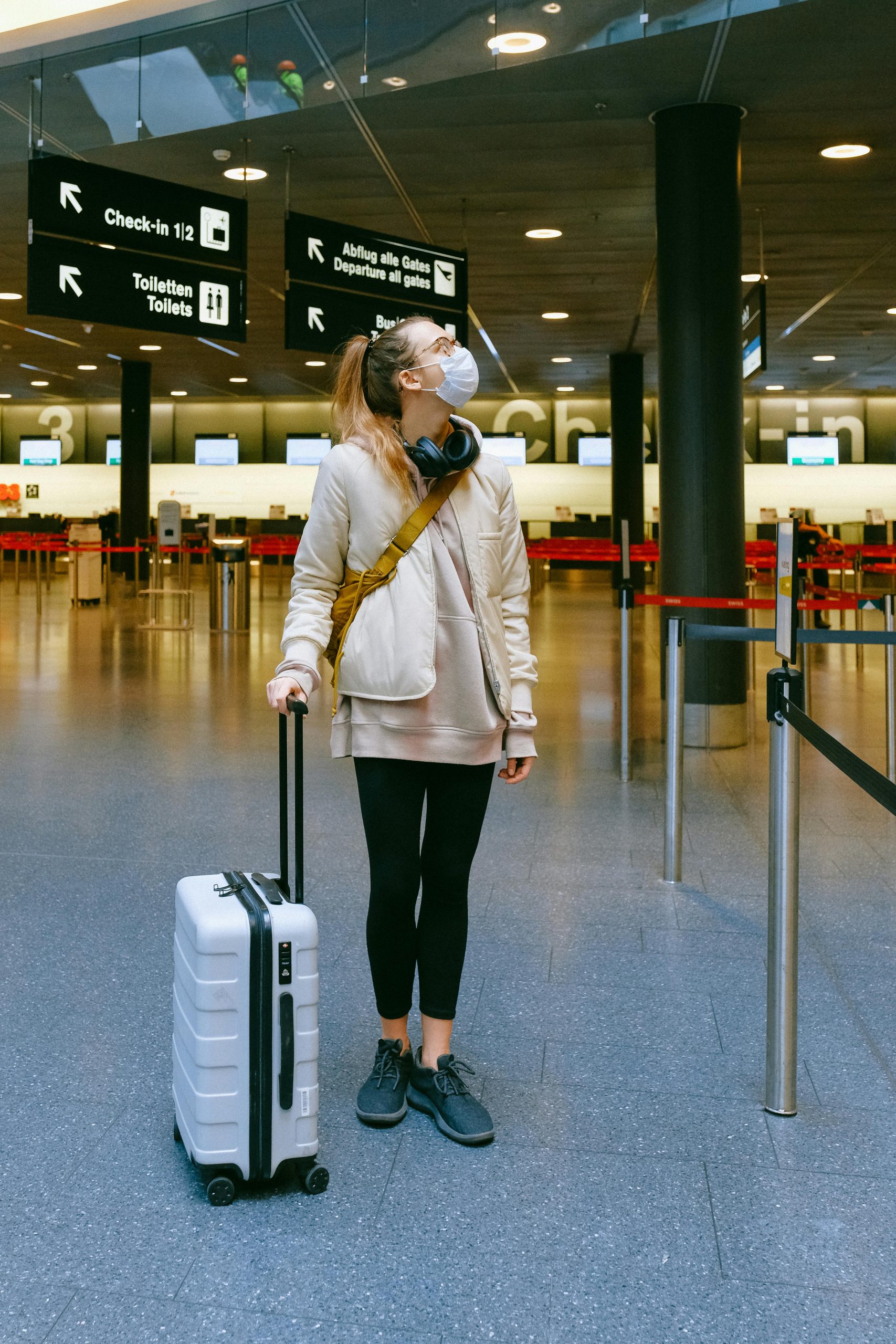 A woman in a face mask stands with her luggage in an empty airport terminal.